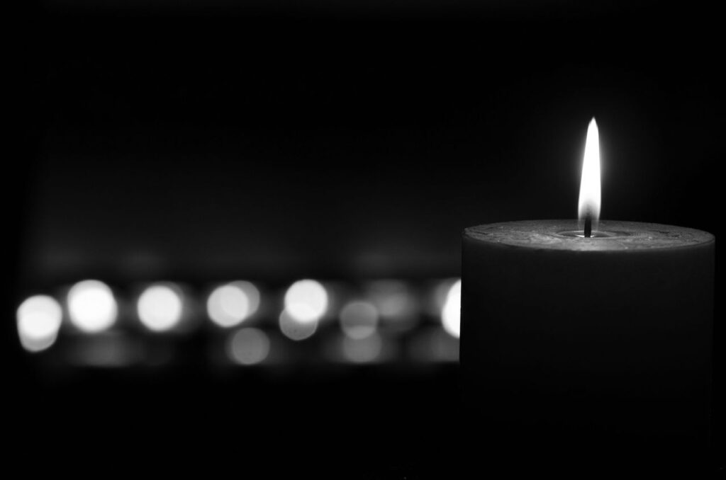 A close-up of a lit candle with a soft glow, captured in black and white for a moody, serene atmosphere.